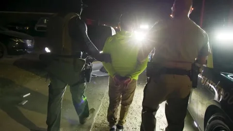 U.S. law enforcement agents escort a cuffed person to a waiting police vehicle Stock Footage 334177210