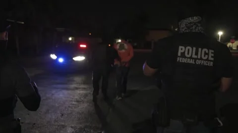 U.S. law enforcement agents escort a cuffed person to a waiting police vehicle Stock Footage 334177239