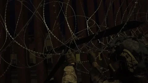 U.S. Marine securing barbed wire to the Mexican border fence during the night Stock Footage 300261352