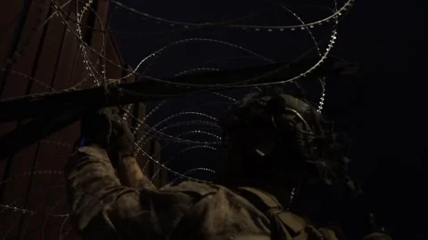 U.S. Marine securing razor wire to the Mexican border fence during the night Stock Footage 300261360