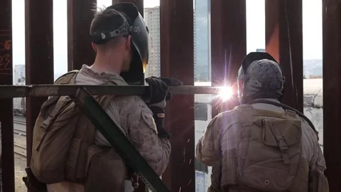 U.S. Marine welding a post to the Mexican border wall to support razor wire Stock Footage 300344870