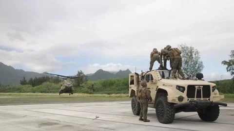 U.S. Marines standing on cab of JLTV with CH-47 Chinook landing nearby Stock Footage 263888126