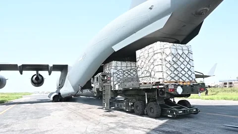 U.S. military pallet loader offloading crates of humanitarian aid from C-17 Stock Footage 209492176