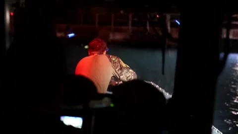 U.S. Navy explosive ordnance disposal sailor pulling cable onto boat at night Stock Footage 201074925
