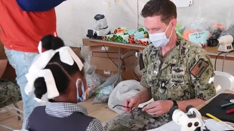 U.S. Navy medic adjusts and gives child eye glasses at medical site Vidéo 227138294