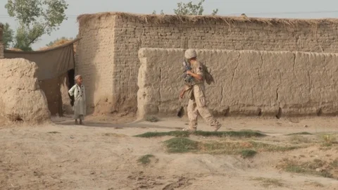 US soldier approaching a small boy on the outskirts of a house in Afghanistan Stock Footage 85746838