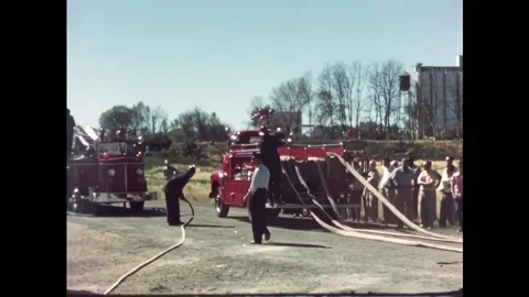 USA - 1950s - Firemen pull hoses from fire trucks and raise a ladder. They spray Stock Footage 327738688