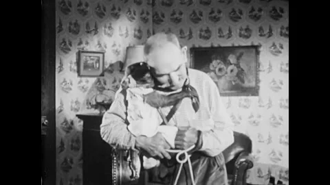 USA - 1955 - A man stands with a monkey in a room. He sits down in a comfy chair 스톡 동영상 327744158