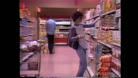 USA - 1984 - Grocery shoppers study nutrition labels at the store and a woman Stock Footage 288080130