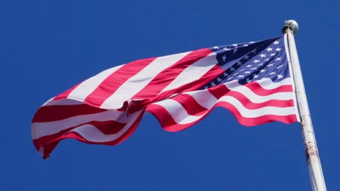 USA flag on a flag pole blowing in the wind against deep blue sky Stock Footage 303270872