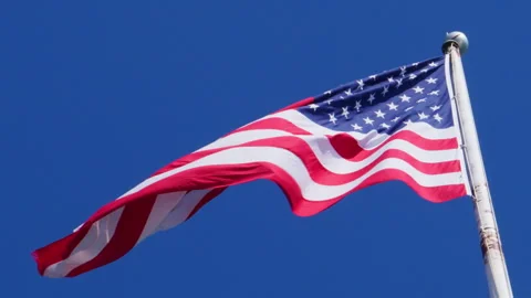 USA flag on a flag pole blowing in the wind against deep blue sky Stock Footage 303271089