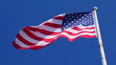 USA flag on a flag pole blowing in the wind against deep blue sky Stock Footage 303313231
