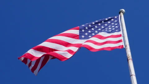 USA flag on a flag pole blowing in the wind against deep blue sky Stock Footage 303313383