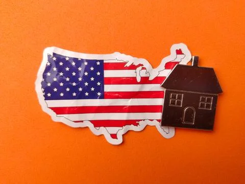 USA flag patterned map sticker with a small metal house model on an orange .. Stock Photos