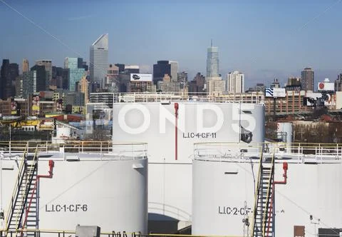 USA, New York City, Oil storage tanks in refinery with Manhattan skyline in Stock Photos