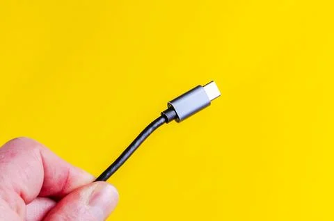USB-C cable held in hand against a bright yellow background Stock Photos