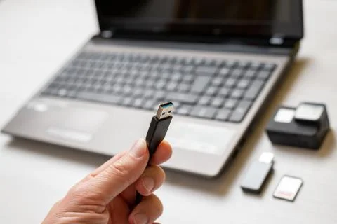 USB cable in hand close-up. Action camera and laptop in background. Concept o Stock Photos