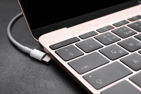 USB cable with lightning connector and laptop on black table, closeup Fotos Stock