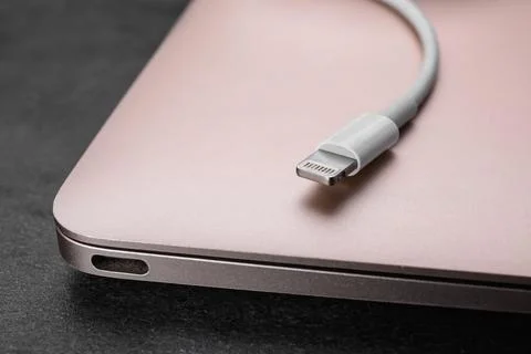 USB cable with lightning connector and laptop on black table, closeup Fotos Stock