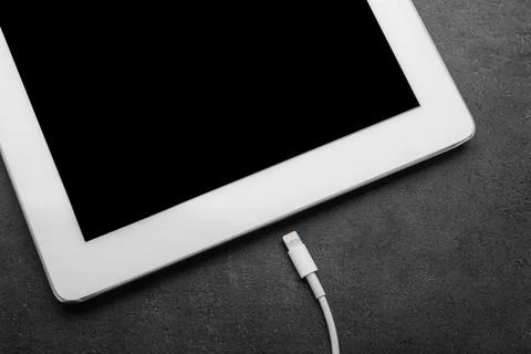 USB cable with lightning connector and tablet on dark table, closeup Fotos Stock
