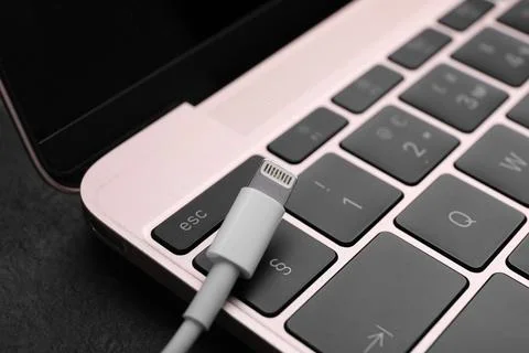 USB cable with lightning connector and laptop on black slate table, closeup Fotos Stock