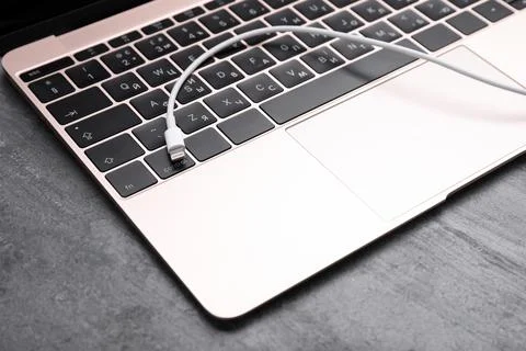 USB cable with lightning connector and laptop on grey table, closeup Fotos Stock
