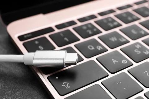 USB cable with type C connector and laptop on grey table, closeup Fotos Stock