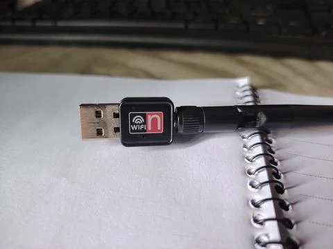 USB WiFi adapter on a spiral notebook next to a pen on a desk with a keyboa.. Stock Photos