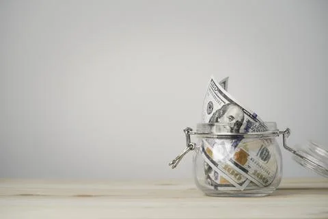 USD dollar banknote roll inside of saving jar on wooden table and copy space Stock Photos