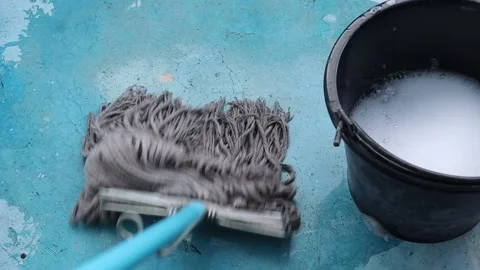 Use a mop near the black plastic bucket to clean the cement floor Stock Footage 163073707