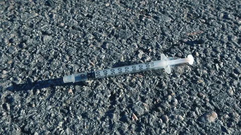 Used Hypodermic Needle Syringe Lying on Asphalt Ground Stock Footage 332628557