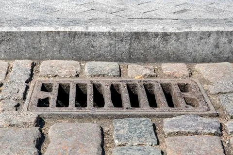 Used iron rectangular manhole drainage system on the old cobbled road. Stock Photos