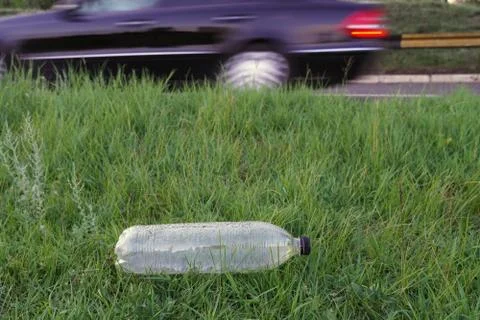 Used plastic bottle as garbage on the grass near road and car, pollution conc Stock Photos