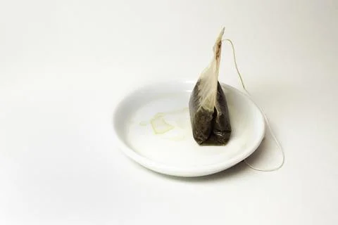 Used tea bag with a long thread, on a small white saucer with tea stains Stock Photos