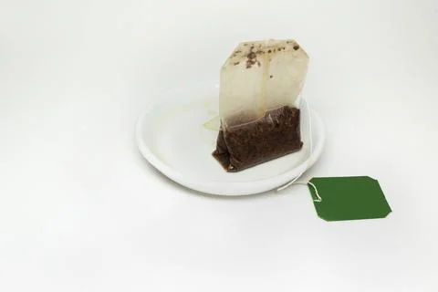 Used tea bag with a long thread and paper green lable, on a small white sau.. Stock Photos