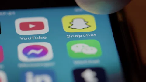 User closes app folder to open yellow Snapchat app on mobile phone screen Stock Footage 300754044
