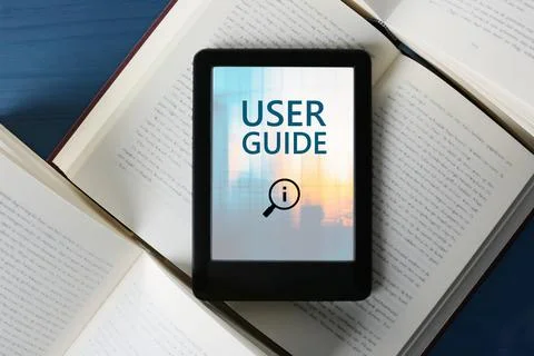 User Guide document open in e-book device and different books on blue woode.. Stock Photos