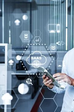 User interacts with mobile device while monitoring SaaS on screen in office.. Stock Photos