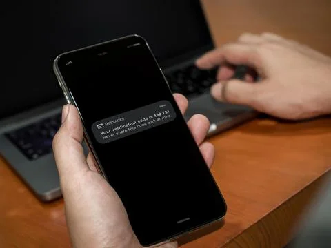 User receives verification code on a smartphone screen while using laptop. .. Фото