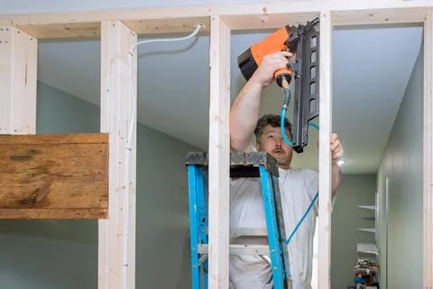 Using an air hammer, a builder nails wooden beams to the frameworks of housing Foto stock