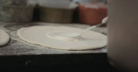 Using the back of a spoon to spread out cream sauce on pizza dough Stock Footage 105309116