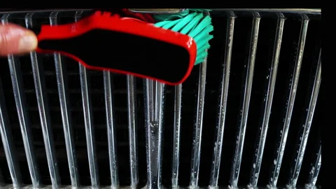 Using a brush and soapy water to clean the chrome grill of an old car. Video stock 221242890