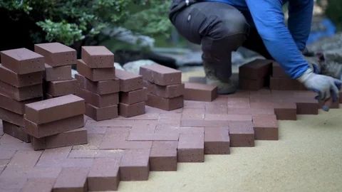 Using the butt of his trowel, a hardscaper taps the red brick pavers into place 库存影片 81993871