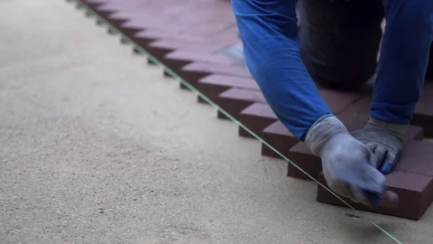 Using the butt of his trowel, a hardscaper taps the red brick pavers into place 库存影片 82001845
