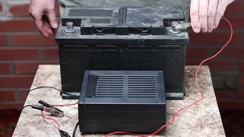 Using car battery charger, user attaches alligator clips to terminals. Stock Footage 224875859