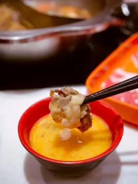 Using chopsticks dip meat in to raw egg. Eating hotpot shabu style. Foto stock