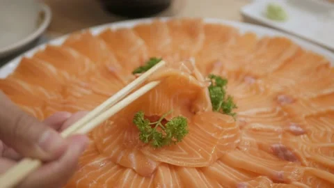 Using chopsticks pick a piece of raw fresh salmon sashimi in japanese restaur Stock Footage 219999347