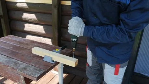 Using a cordless drill driver to drive screws into a wooden board on an out.. Stock Photos