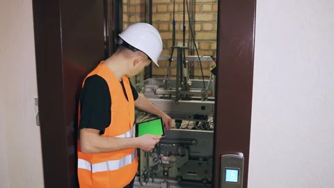 Using a digital tablet, the engineer regulates the elevator security system. A Stock Footage 266229799