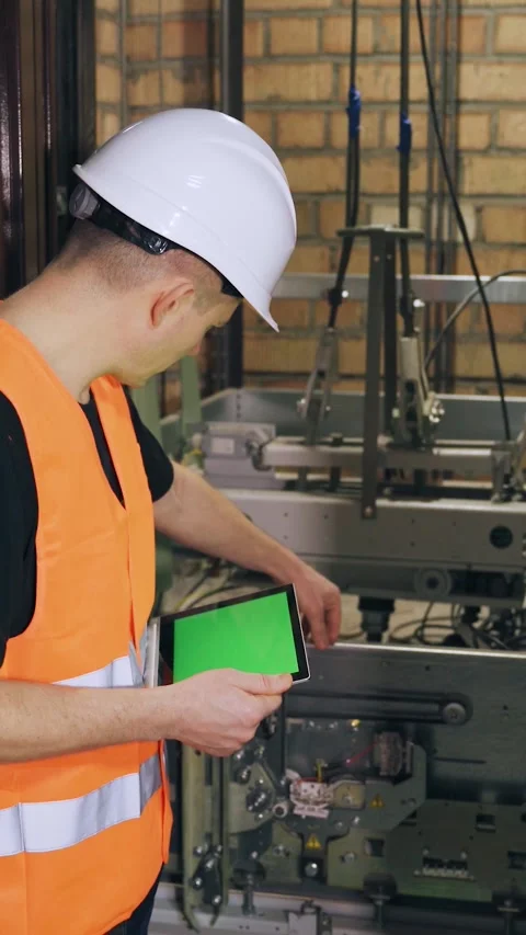 Using a digital tablet, the engineer regulates the elevator security system. A Stock Footage 300877874